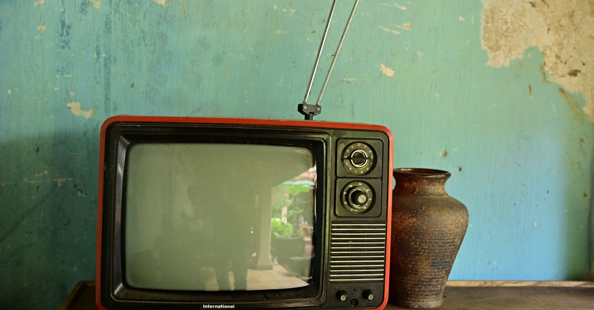 A vintage television with antenna beside a ceramic vase on a worn wooden surface against a rustic wall.